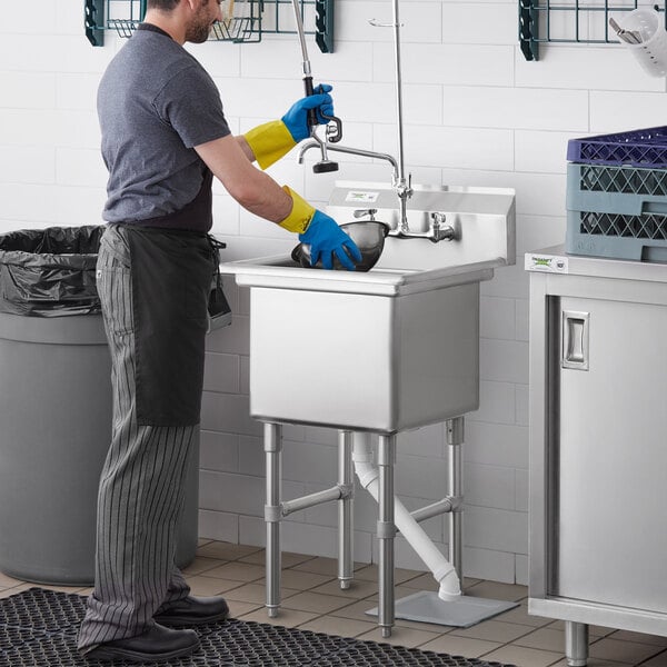 A man wearing blue and yellow gloves washing a Regency stainless steel sink.