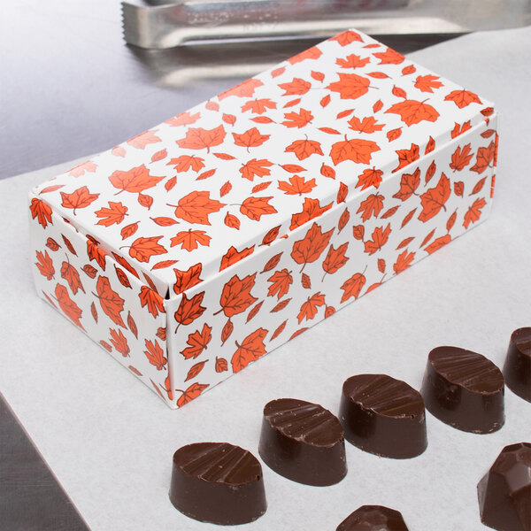 A 1/2 lb. Leaf Candy Box with orange leaves on the counter next to chocolates.