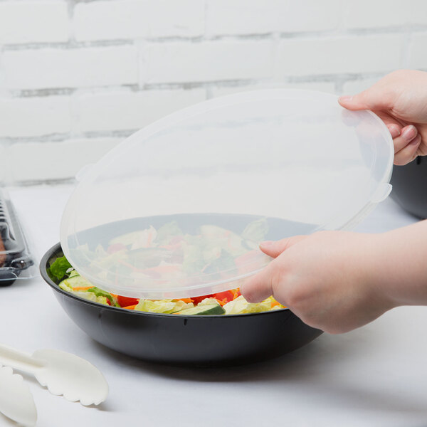 A person using a Fineline clear plastic lid to cover a bowl of salad.