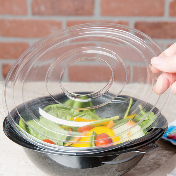 A hand using a Fineline clear plastic flat lid to cover a bowl of salad.