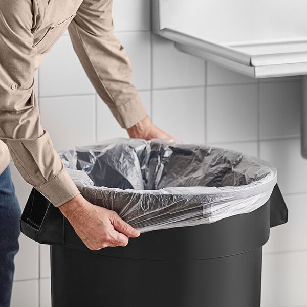 A person putting a Lavex trash bag in a trash can.