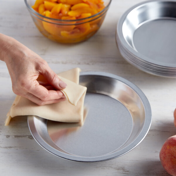 A hand using a cloth to wipe a Chicago Metallic aluminum pie pan on a counter.