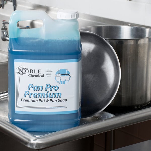 A blue plastic jug of Noble Chemical Pan Pro concentrated soap on a counter next to a pan.