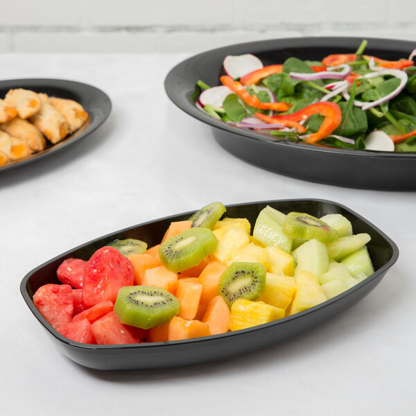 A bowl of salad with vegetables in a black Fineline Luau bowl on a table.