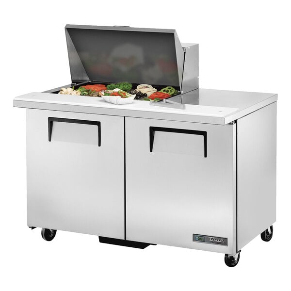 A True stainless steel refrigerated sandwich prep table with two doors on a counter with a food tray.