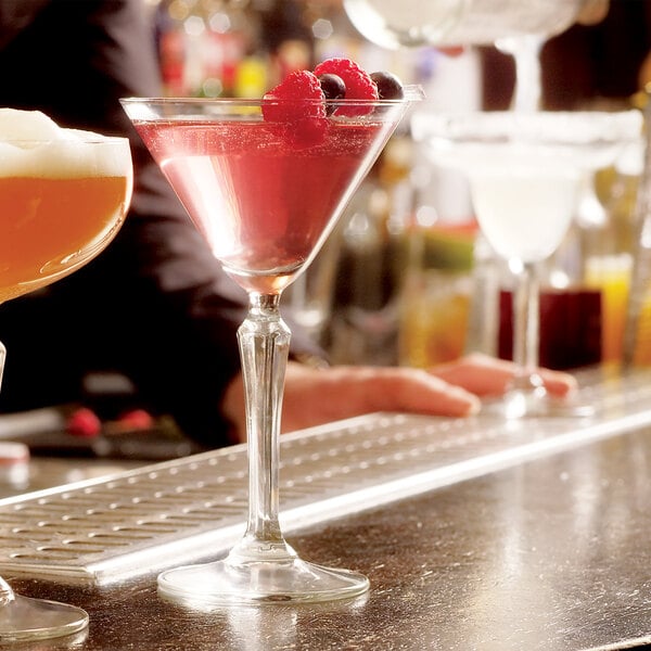 A bartender pouring pink drinks into Libbey martini glasses on a bar.