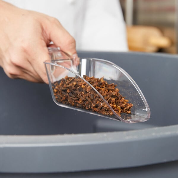 A hand holding a Cambro clear polycarbonate scoop of cloves.