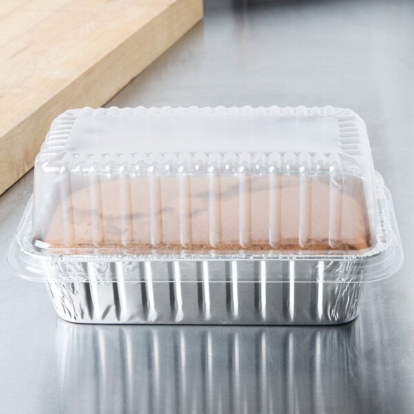 A Durable Packaging foil bread loaf pan with a clear plastic lid containing a loaf of bread.