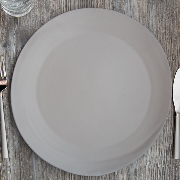 A 10 Strawberry Street matte gray stoneware charger plate with a knife and fork on a wooden table.