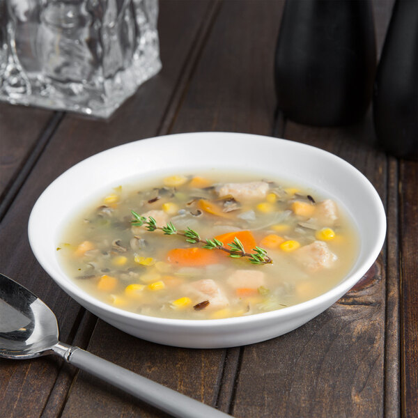 A white 10 Strawberry Street stoneware bowl filled with chicken, corn, and vegetable soup with a spoon.