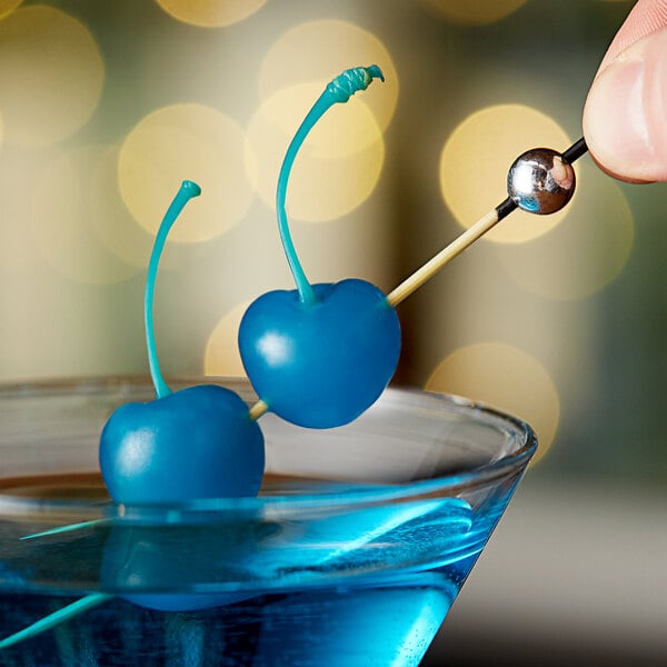 A blue martini garnished with Regal Dark Blue Maraschino Cherries with Stems.