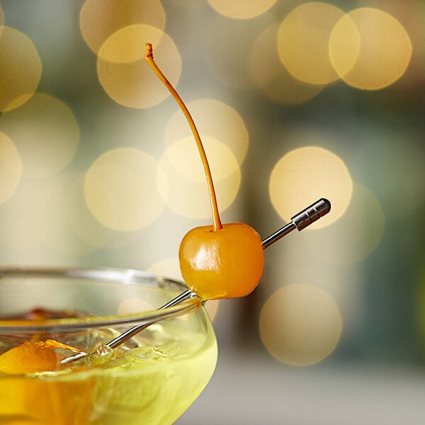 A glass of orange juice on a table in a cocktail bar with a yellow maraschino cherry on the rim.