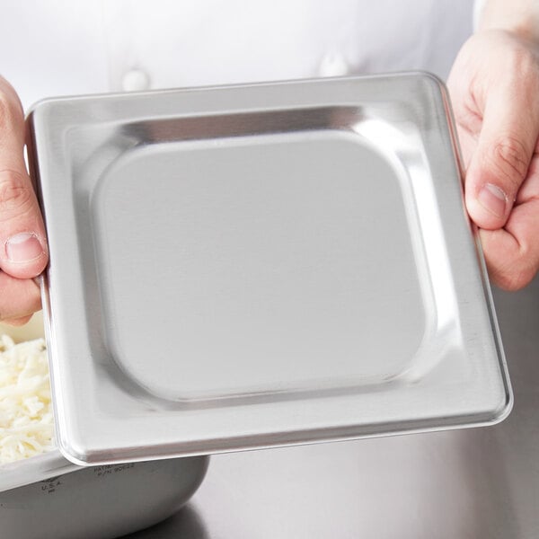 A person holding a silver square pan cover.