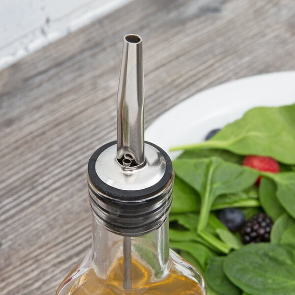 A Choice oil cruet bottle with a metal tip next to a plate of salad.