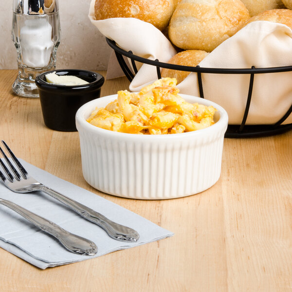 A Tuxton eggshell fluted ramekin filled with macaroni and cheese on a table with a basket of bread.