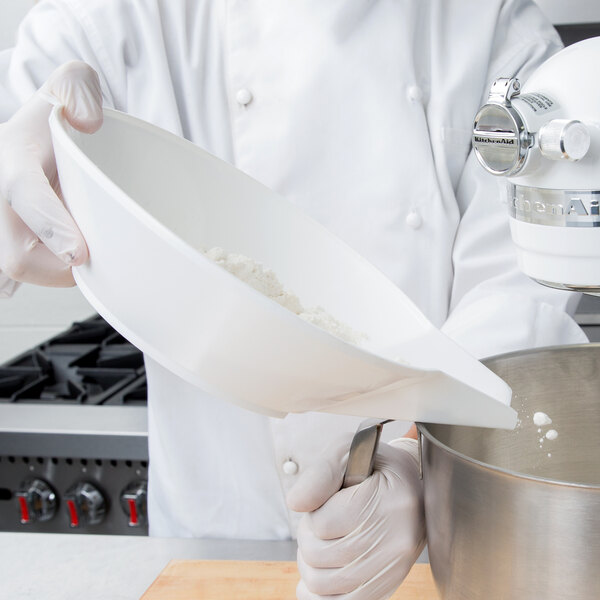 A person using a Cardinal Detecto white plastic scale scoop to pour flour into a bowl.