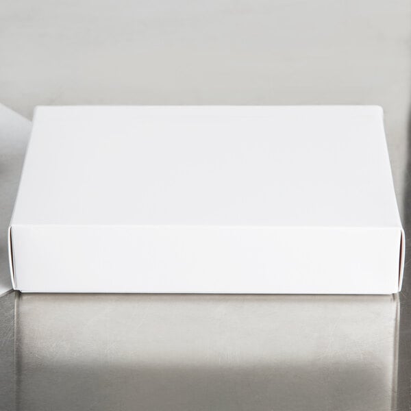 A 9 3/8" x 6" white candy box with a white lid on a white table.
