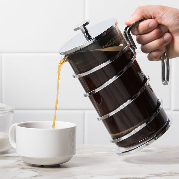 A hand pouring coffee into a Libbey stainless steel French press.