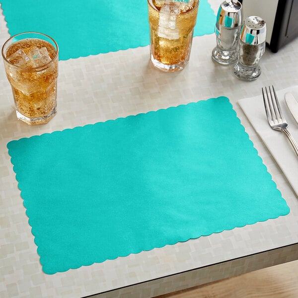 A teal scalloped paper placemat on a table with a glass of ice tea and a glass of ice water.