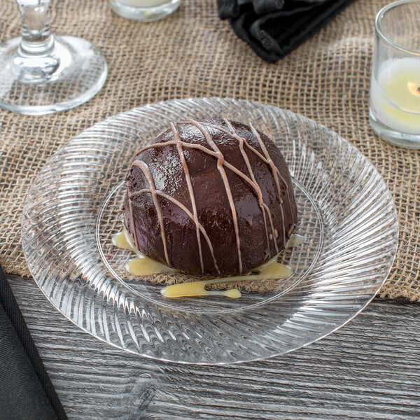 A round chocolate dessert on a Visions clear plastic plate with white stripes.