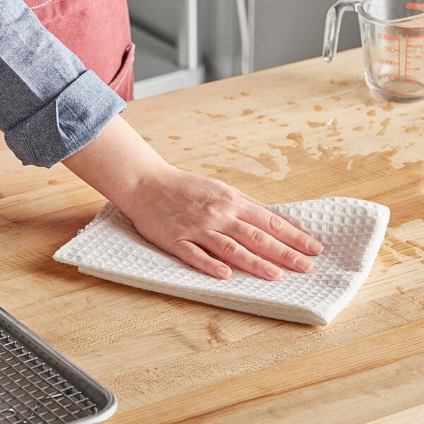 A person using a Choice natural waffle-weave kitchen towel to clean a wooden table.