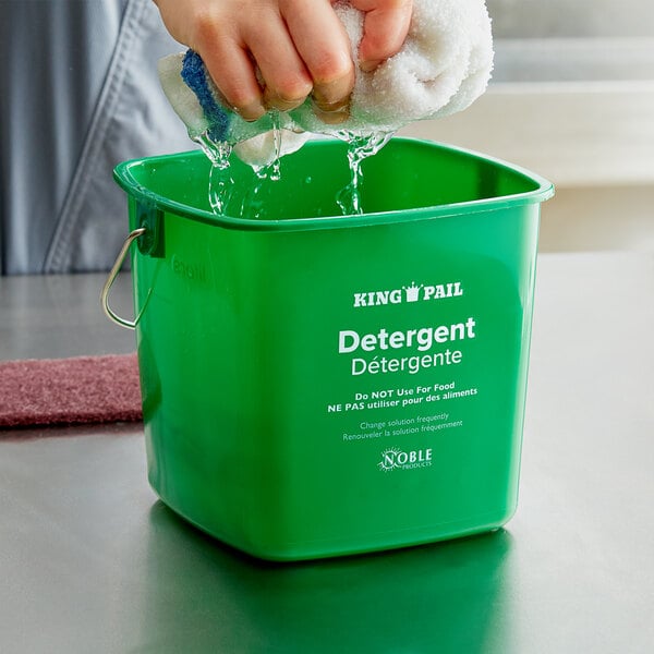 A person washing a green Noble Products cleaning pail on a counter.
