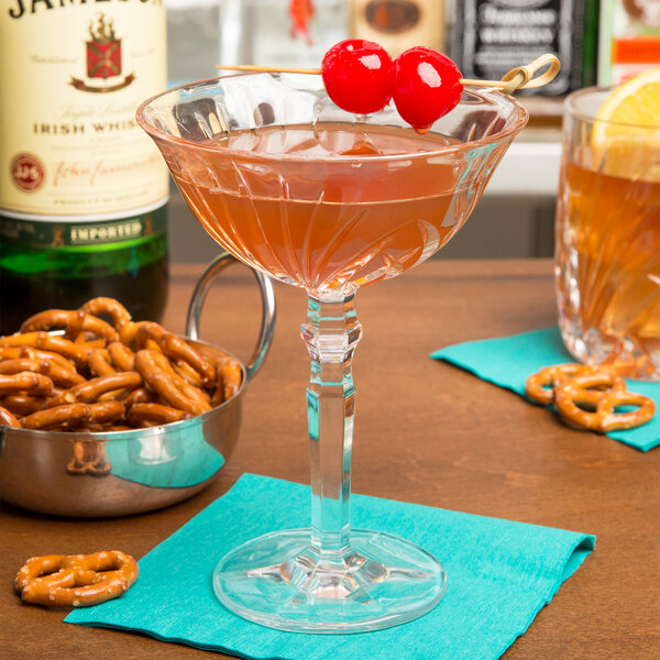 A Nachtmann cocktail glass filled with a brown drink, cherries, and a bowl of pretzels.