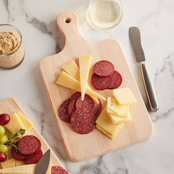 A Choice wooden serving and cutting board with meat and cheese on it on a table.