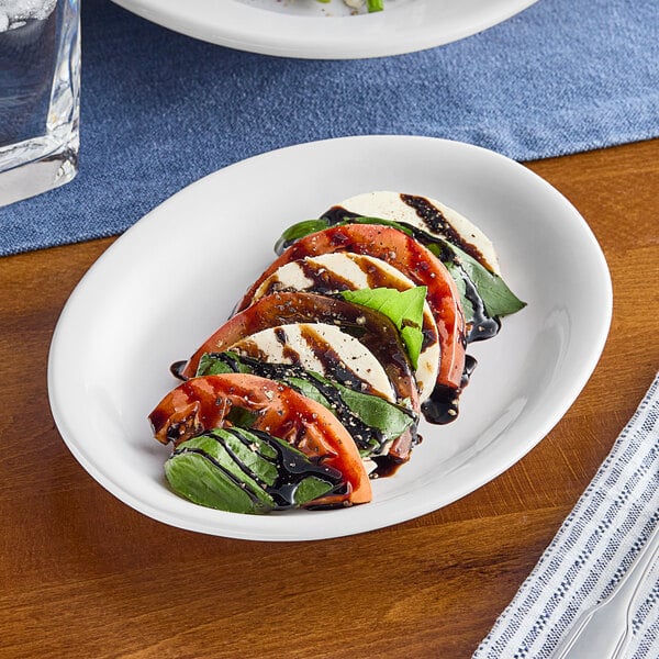 An Acopa Bright White oval stoneware platter with food on a table.