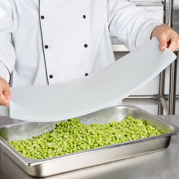 A chef using a Flexsil high-heat silicone lid to cover a metal steam table pan of green beans.