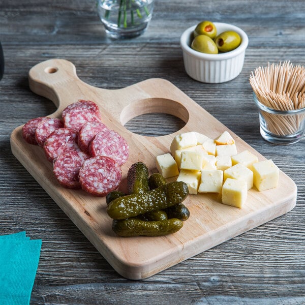 A Choice wooden serving and cutting board with food on it, including cubes of cheese and a ramekin of green olives.