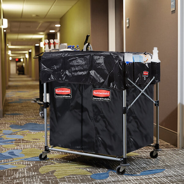 A black Rubbermaid laundry cart with a black cover on it and extra black bags inside.