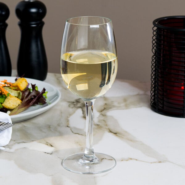 A Reserve by Libbey wine glass filled with white wine on a table with a salad.