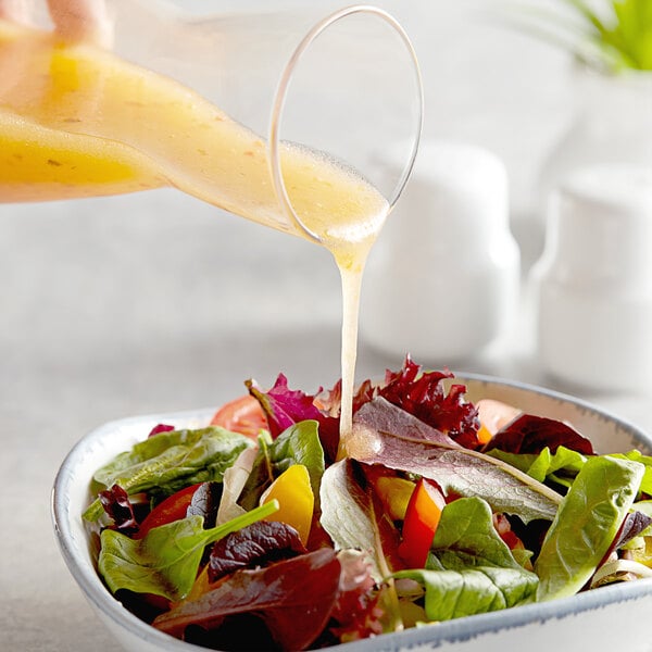 A person pouring Hidden Valley Golden Italian Dressing into a bowl of salad.