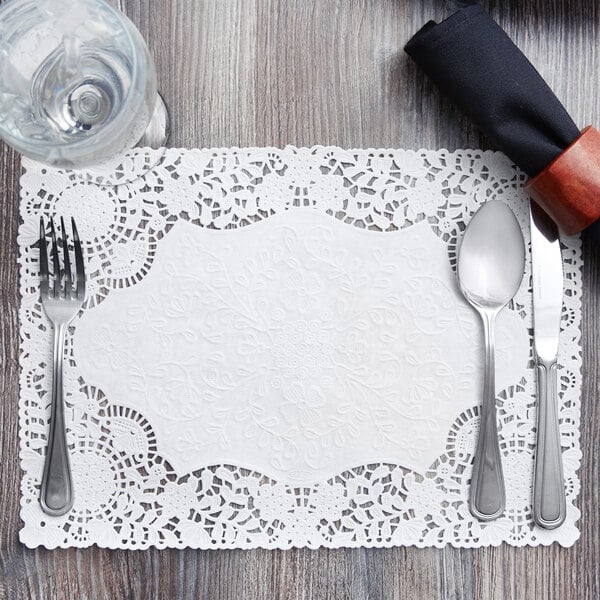 A white floral lace paper placemat with a silver fork and knife on it.