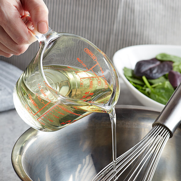 A hand pouring 100% Pure Organic Canola Oil from a measuring cup into a bowl.