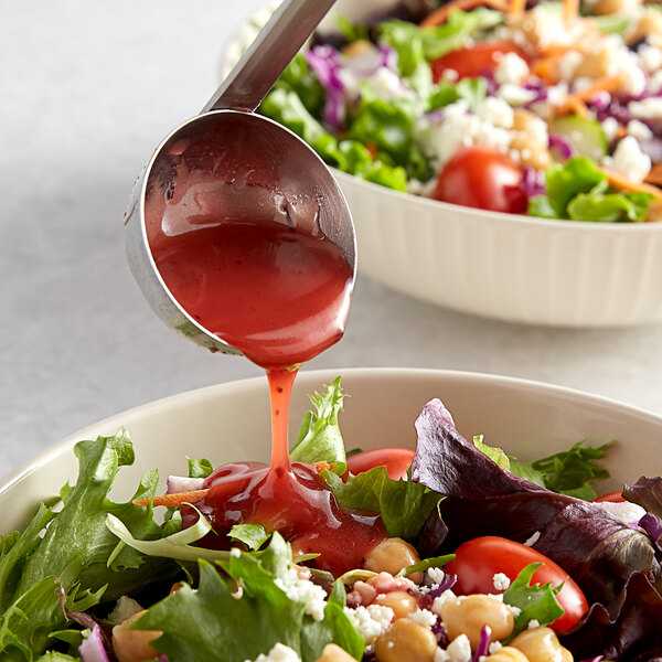 A bowl of salad with Hidden Valley Raspberry Vinaigrette being poured over it with a spoon.