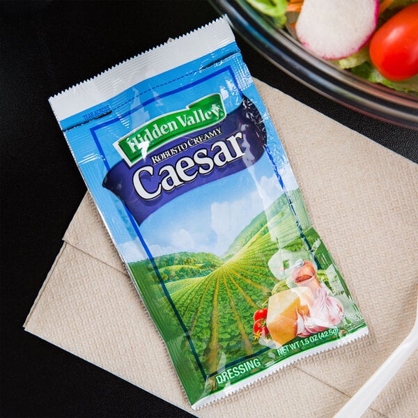 A bowl of salad with a packet of Hidden Valley Creamy Caesar dressing on a napkin.