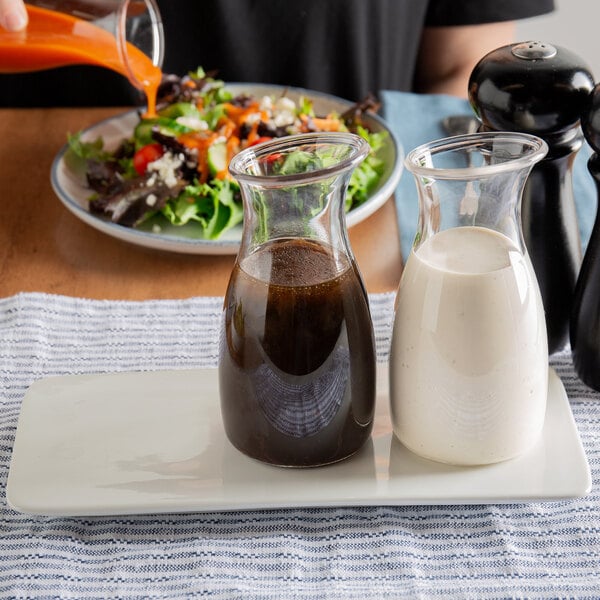 A person pours Hidden Valley Balsamic Vinaigrette into two glass containers on a table with a plate of salad.