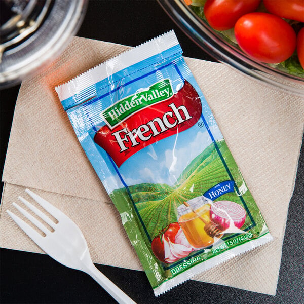 A bowl of tomatoes and lettuce with a packet of Hidden Valley French Dressing on a napkin.