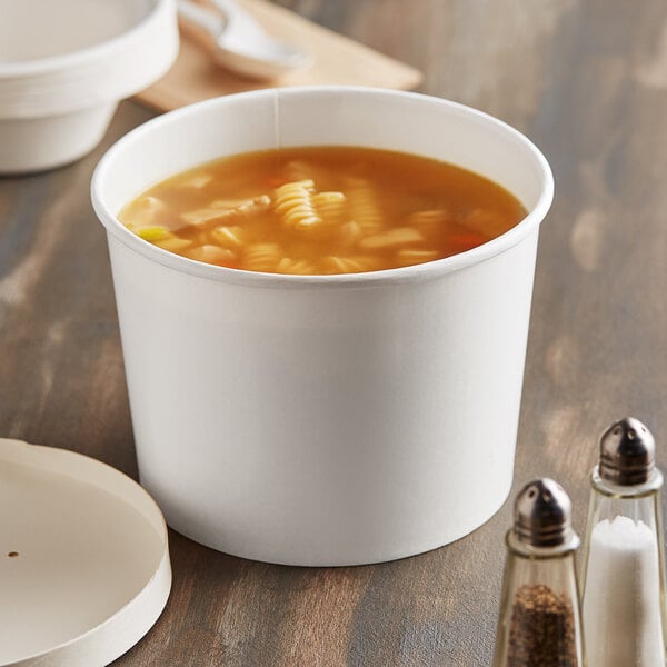 A white paper bowl of soup with a brown edge on a table.