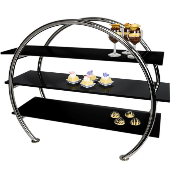A black stainless steel 3 tier circular display stand with black acrylic shelves holding desserts on a counter.