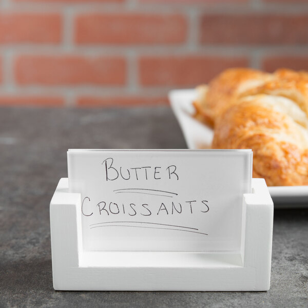 A white Cal-Mil U-frame table sign holding a white sign with black lettering next to a plate of butter croissants.