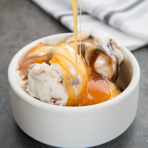 A bowl of ice cream with HERSHEY'S caramel sauce being poured over it.