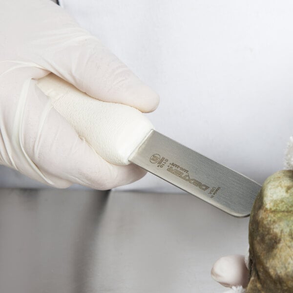 A person in white gloves uses a Dexter Russell clam knife to cut a rock.