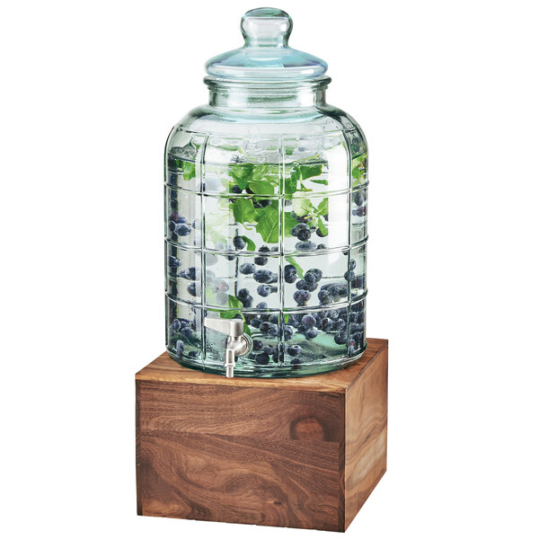 A Cal-Mil glass beverage dispenser with a jar of blueberries and leaves inside.