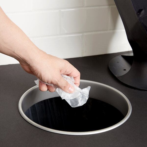 A hand holding a plastic bag over a round hole in a counter.