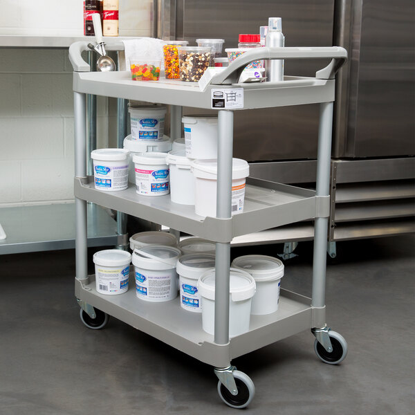 A Rubbermaid platinum plastic utility cart with food containers and white buckets on it.