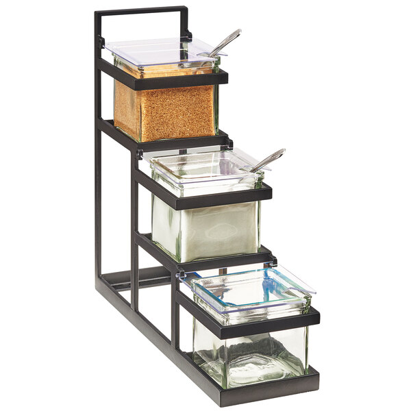 A black metal Cal-Mil rack with 3 glass containers on a counter.