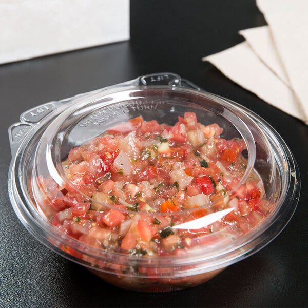 A Dart clear plastic bowl filled with salsa on a table.
